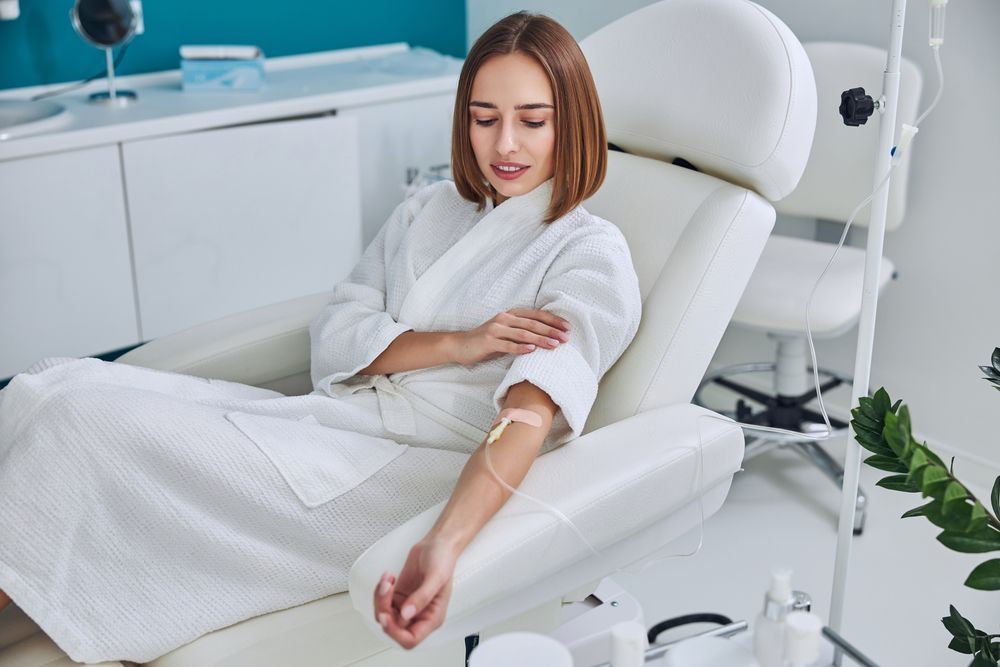 Person reclining in a white salon chair, holding an arm out during a treatment in a bright spa room